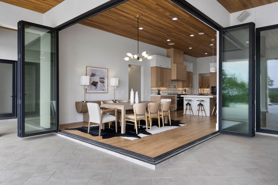 Expansive folding glass doors open to reveal an open-concept living space with light wood flooring and a wooden plank ceiling