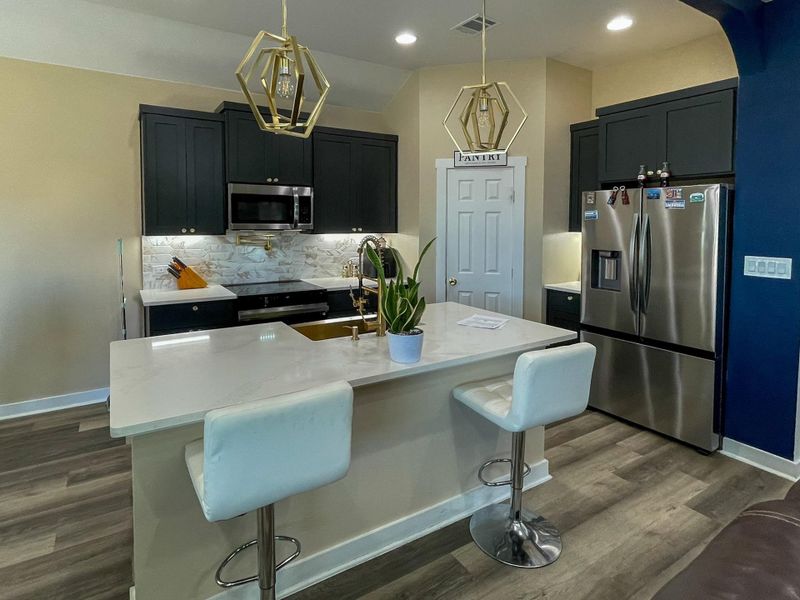 Kitchen featuring stainless steel appliances, a breakfast bar, dark cabinets, tasteful backsplash, and decorative light fixtures