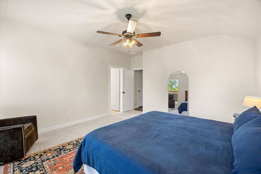 Carpeted bedroom featuring ceiling fan, arched walkways, and vaulted ceiling