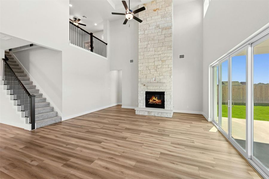 Unfurnished living room with a towering ceiling, light wood-type flooring, a stone fireplace, ceiling fan, and stairs