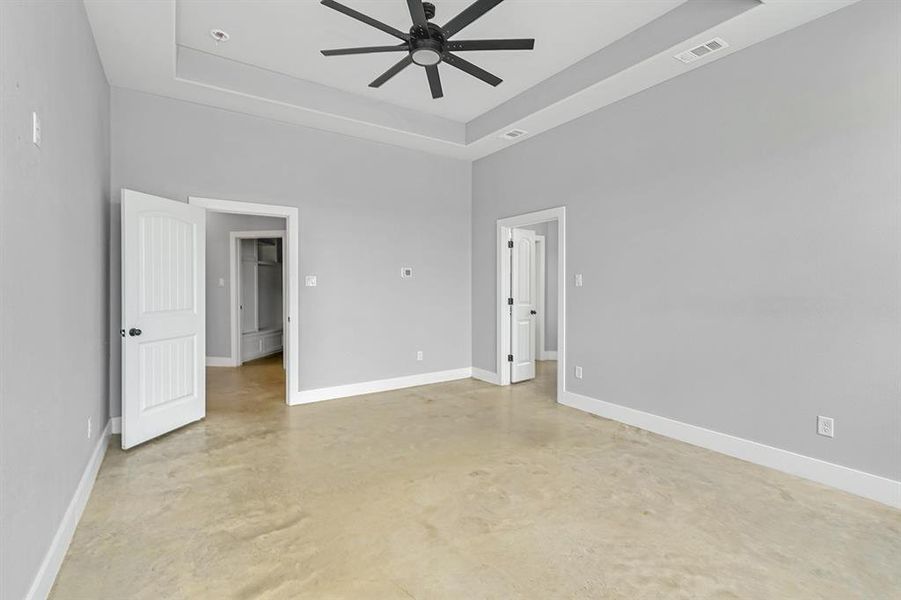 Empty room with concrete flooring, ceiling fan, a tray ceiling, baseboards, and a high ceiling
