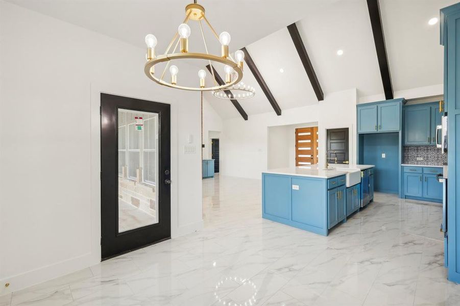 Kitchen featuring hanging light fixtures, an inviting chandelier, beamed ceiling, blue cabinets, and backsplash