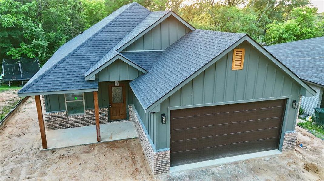 View of front of home with roof with shingles, a trampoline, a garage, board and batten siding, and a porch