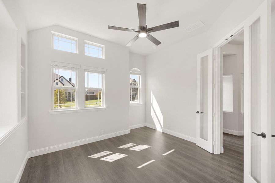 Empty bedroom with dark hardwood floors, ceiling fan, vaulted ceiling, and multiple windows with natural light Empty bedroom with dark hardwood floors, ceiling fan, vaulted ceiling, and multiple windows with natural light