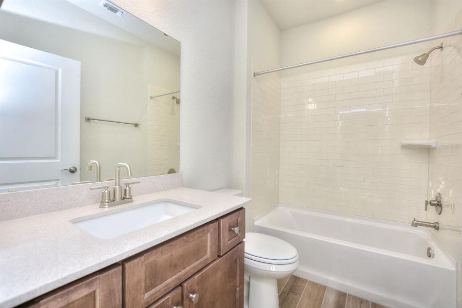 Bathroom featuring visible vents, shower / washtub combination, toilet, wood finished floors, and vanity