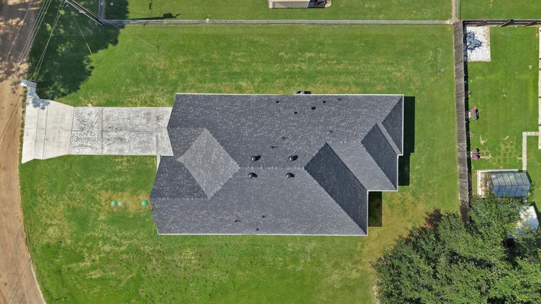 Spacious lot featuring a dark shingle roof, green lawn, and a light-colored concrete driveway