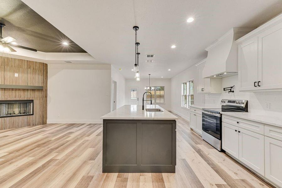 Kitchen with white cabinetry, stainless steel electric stove, pendant lighting, a center island with sink, and recessed lighting Kitchen with white cabinetry, stainless steel electric stove, pendant lighting, a center island with sink, and recessed lighting
