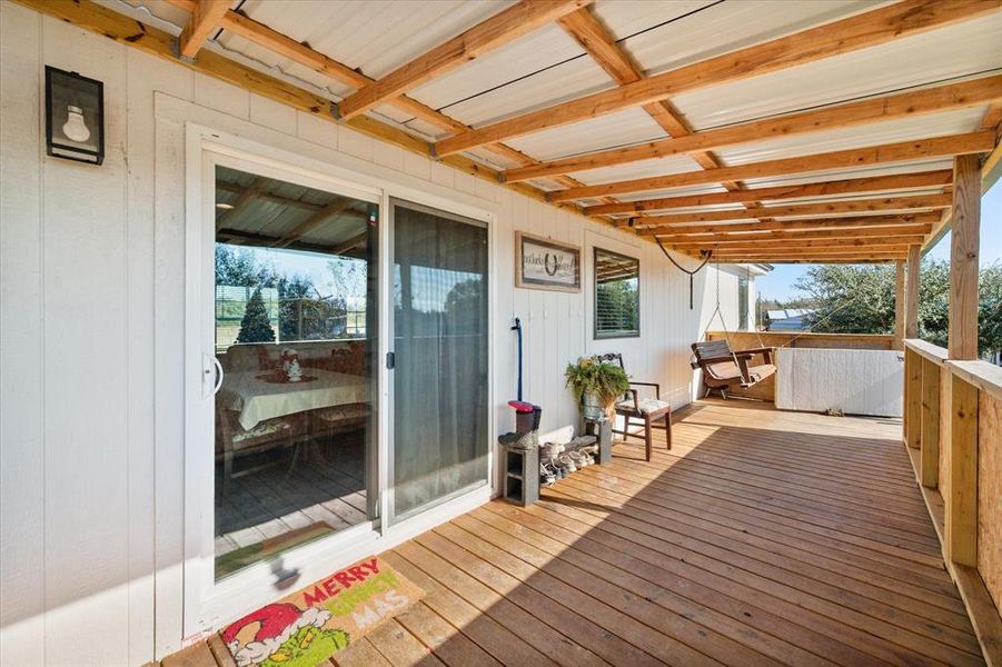 Expansive covered porch featuring wood-finish flooring, exposed wood beams, a corrugated metal ceiling, and a sliding glass door