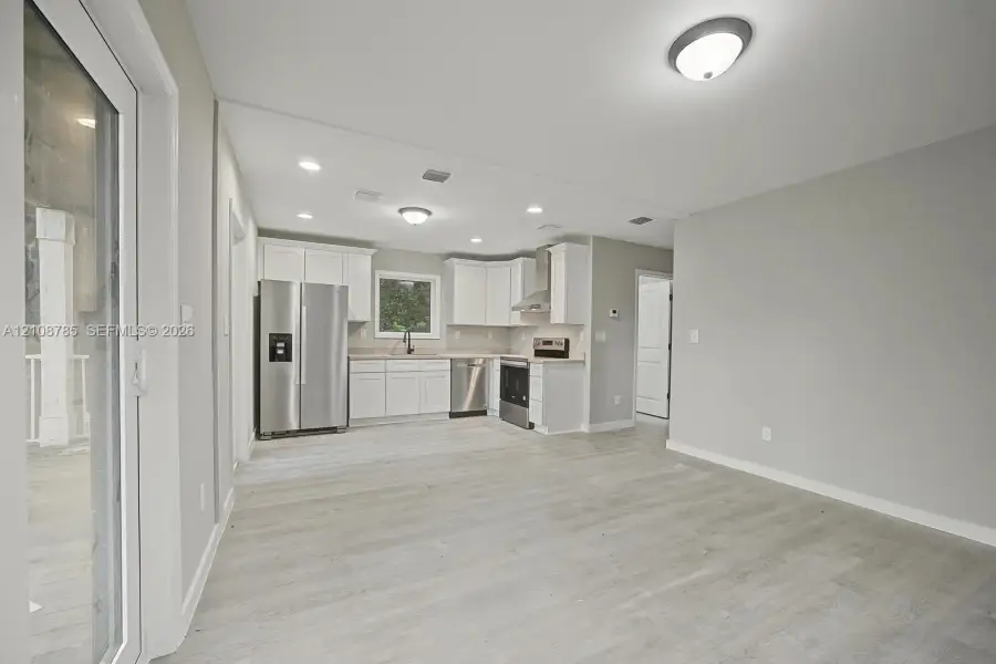 Kitchen featuring white cabinetry, stainless steel appliances, wood-finish flooring, recessed lighting, and a sliding glass door Kitchen featuring white cabinetry, stainless steel appliances, wood-finish flooring, recessed lighting, and a sliding glass door