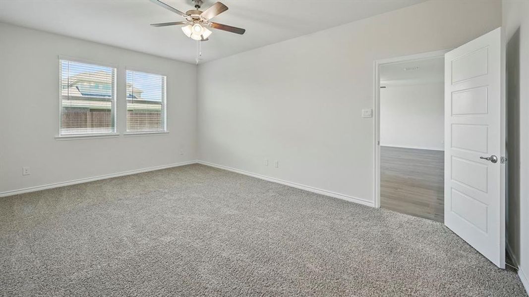 Carpeted room featuring light gray walls, two windows with blinds, a ceiling fan with integrated lighting, and a white interior door with horizontal paneling
