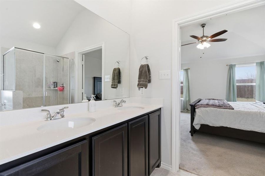 Full bathroom with lofted ceiling, double vanity, ensuite bath, light colored carpet, and a stall shower