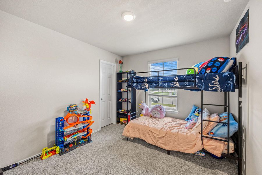 A well-lit bedroom with carpeted floors features a bunk bed and a window with blinds.