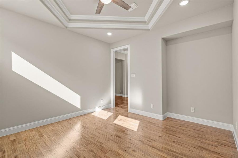 Unfurnished bedroom featuring ornamental molding, light wood-type flooring, ceiling fan, and a tray ceiling