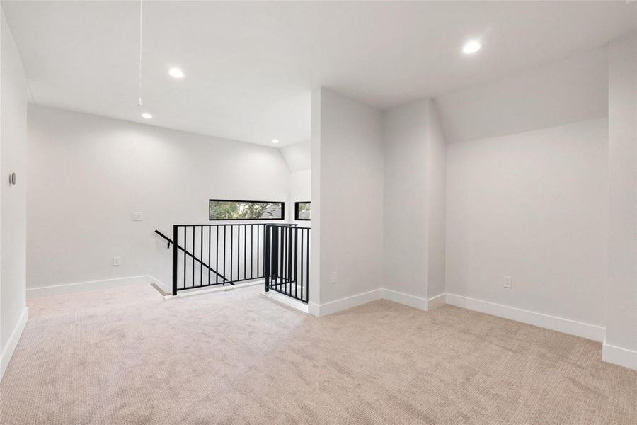 A well-lit upper level space with carpeted flooring features contemporary railing and elevated windows.