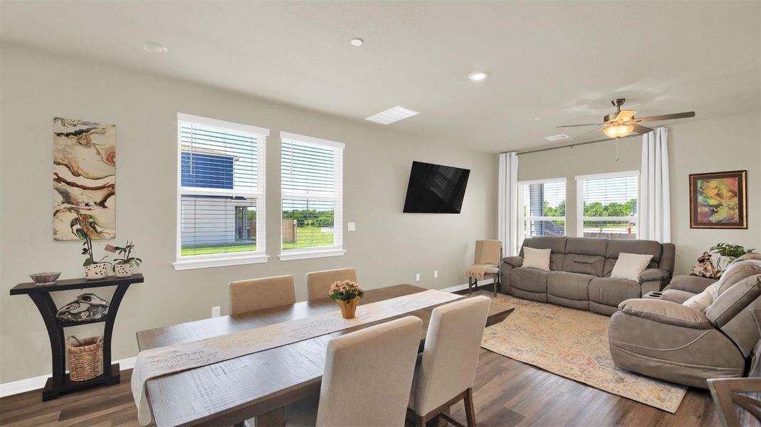 Open-concept living area featuring wood-finish flooring, neutral wall tones, multiple windows with blinds, and a ceiling fan