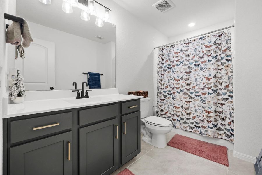 Bathroom featuring a dark gray vanity with gold-tone hardware, a white countertop, and a shower with a patterned curtain