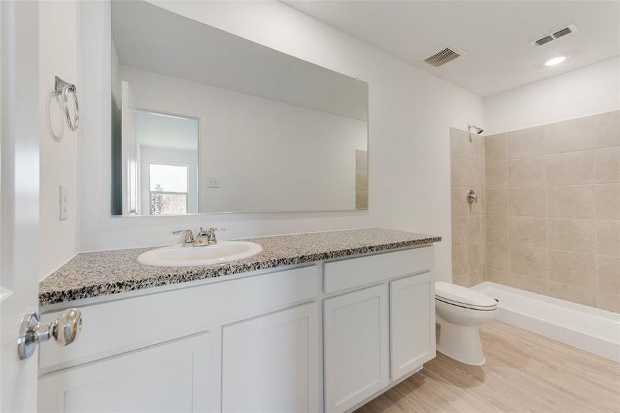 Bathroom featuring wood-type flooring, a tile shower, vanity, and toilet