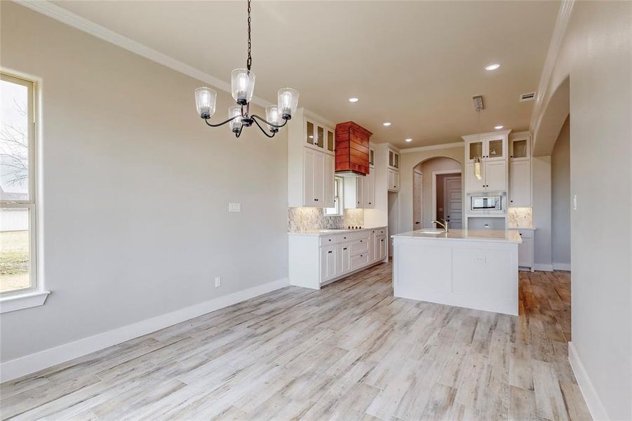 Kitchen with stainless steel microwave, backsplash, hanging light fixtures, white cabinets, and ornamental molding