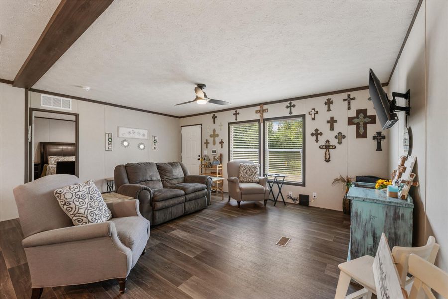 Living room with a textured ceiling, a ceiling fan, dark wood-style flooring, and crown molding