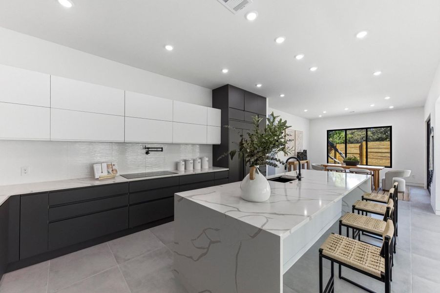 Kitchen with two tone color scheme, modern cabinets, backsplash, light stone countertops, and recessed lighting