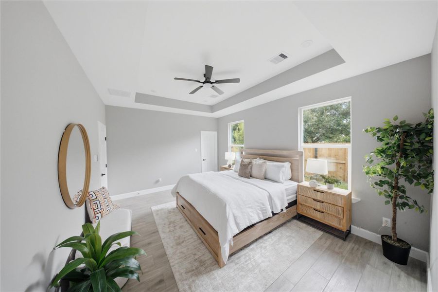Spacious primary bedroom with elegant tray ceiling, abundant natural light, and modern design elements.