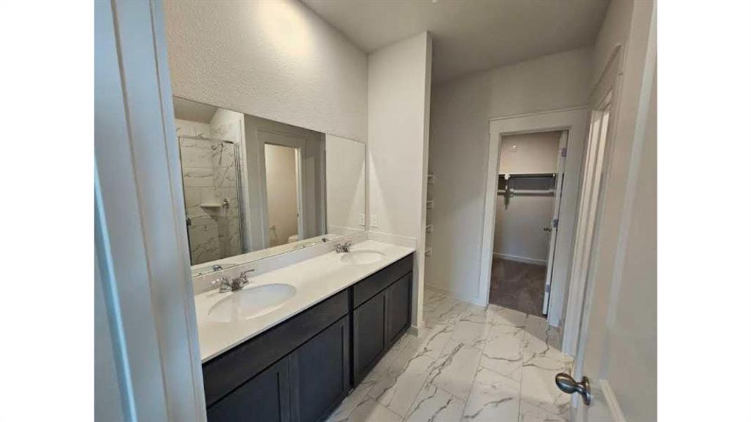 Bathroom featuring a dual vanity with white countertops and dark cabinetry, a frameless wall mirror, and large format white tile flooring with veining Bathroom featuring a dual vanity with white countertops and dark cabinetry, a frameless wall mirror, and large format white tile flooring with veining