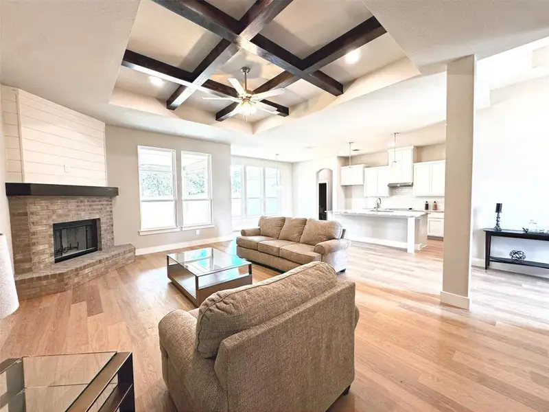 Open-concept living area featuring wood-finish flooring, a tray ceiling with exposed wood beams, and recessed lighting Open-concept living area featuring wood-finish flooring, a tray ceiling with exposed wood beams, and recessed lighting