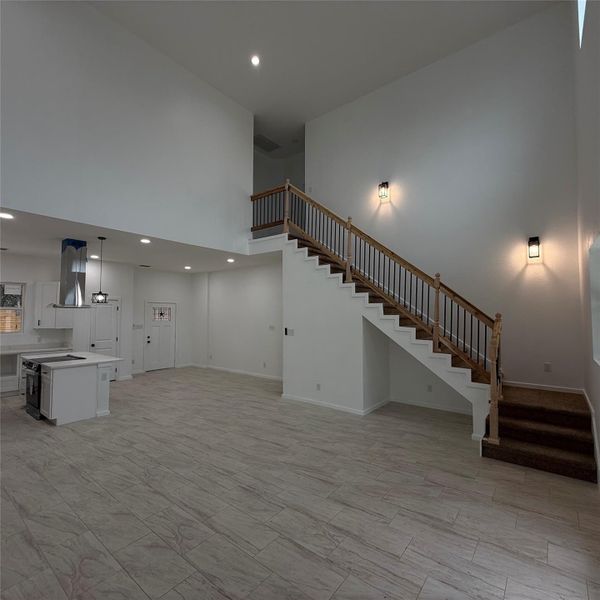 Two-story foyer featuring a wood and wrought iron staircase, wood-finish flooring, recessed lighting, and an open-concept kitchen with white cabinetry