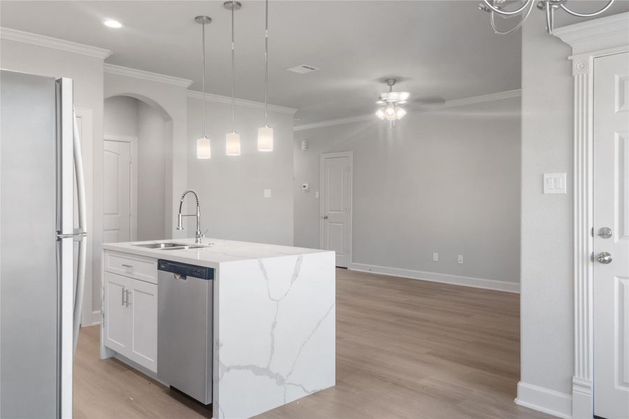 This photo showcases a modern kitchen with a sleek white island featuring a marble countertop and a built-in sink. It includes stainless steel appliances, pendant lighting, and an open layout with light wood flooring, offering a bright and airy ambiance.