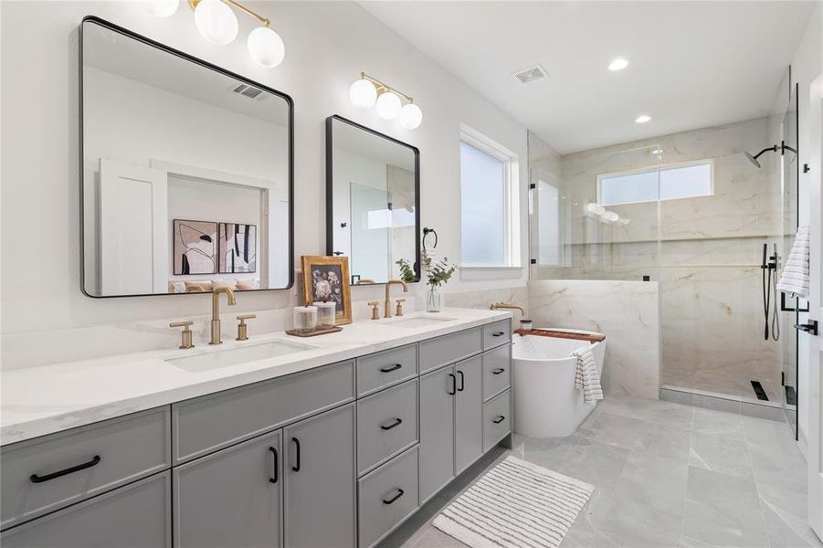 A breathtaking spa-like en-suite bath featuring quartz countertops, dual sinks, a freestanding soaking tub, and a glass-enclosed walk-in shower with designer tile.