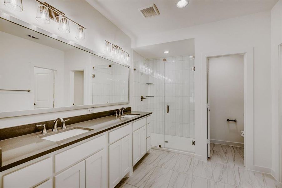 Dual vanity with undermount sinks and dark countertops, alongside a glass-enclosed shower with vertical subway tile
