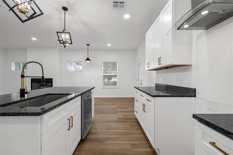 Modern kitchen featuring dark countertops, white cabinetry with bronze hardware, and a black sink with a flexible gold and black faucet Modern kitchen featuring dark countertops, white cabinetry with bronze hardware, and a black sink with a flexible gold and black faucet