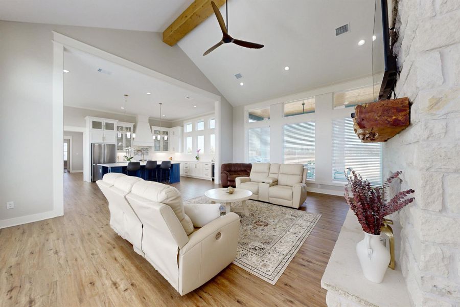 aulted ceilings with an exposed wood beam, contemporary ceiling fan, stone-faced fireplace, recessed lighting, and wood-finish flooring
