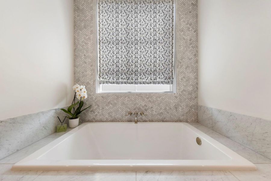 Statement soaking tub surrounded by marble finishes and a textured tile accent wall, designed for relaxation within the primary bathroom..