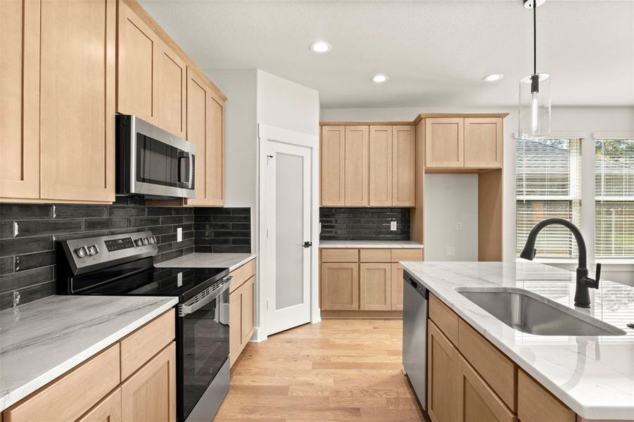 Kitchen featuring appliances with stainless steel finishes, light brown cabinetry, light stone countertops, decorative light fixtures, and recessed lighting