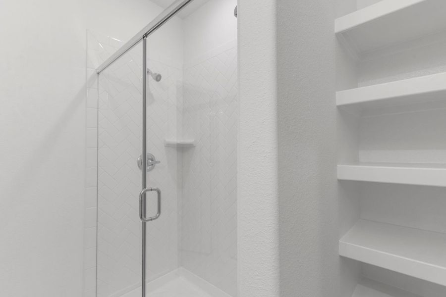 Spa-style walk-in shower with built-in shelving and a frameless glass door, adding both convenience and elegance.