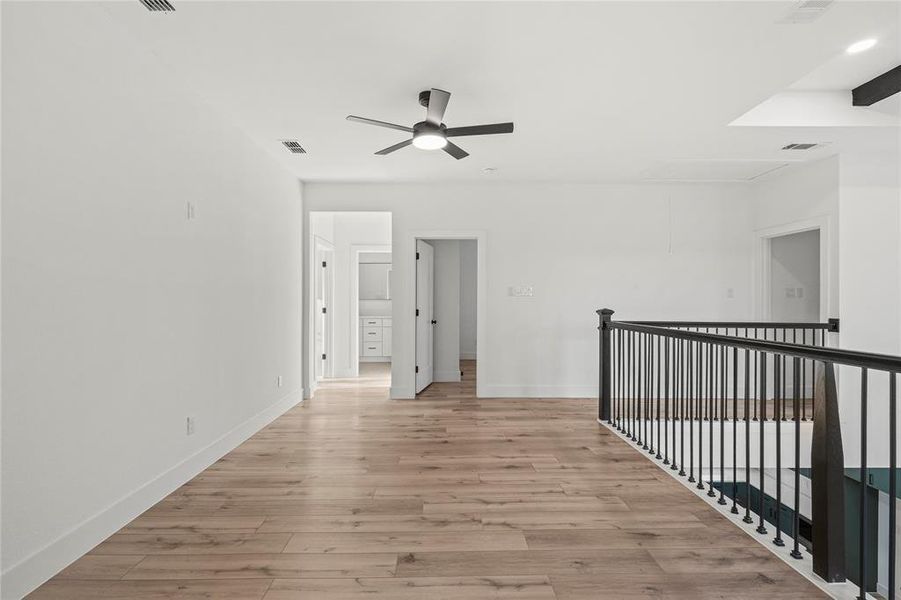Empty room with attic access, light wood-style flooring, and a ceiling fan