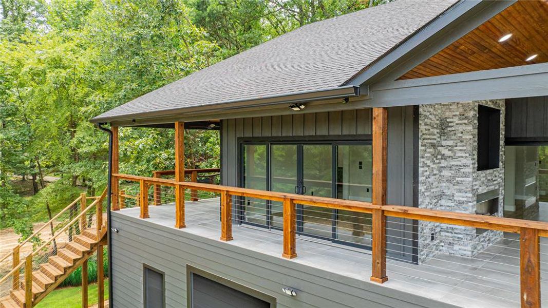 Expansive outdoor deck featuring wood posts, cable railings, and a stone-clad exterior fireplace