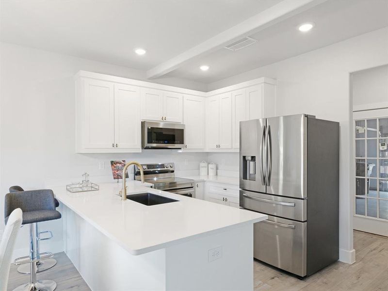 Kitchen with white cabinetry, appliances with stainless steel finishes, a kitchen bar, light hardwood / wood-style floors, and kitchen peninsula