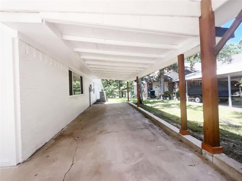 Covered carport featuring a concrete drive, painted brick exterior, and exposed beam ceiling