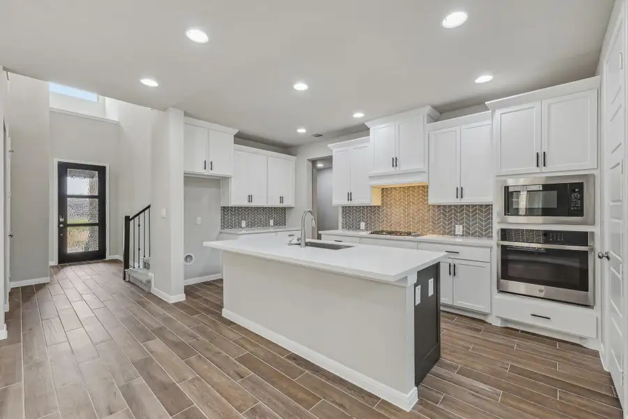 Kitchen with appliances with stainless steel finishes, a sink, dark wood-type flooring, light countertops, and backsplash Kitchen with appliances with stainless steel finishes, a sink, dark wood-type flooring, light countertops, and backsplash