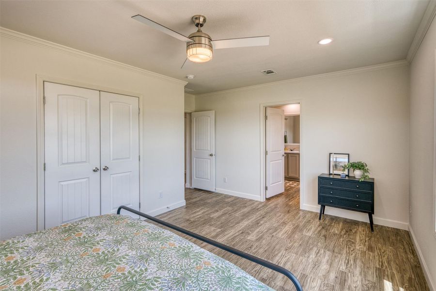 A well-lit bedroom with crown molding, wood-look flooring, and a ceiling fan, offering a tranquil retreat. A well-lit bedroom with crown molding, wood-look flooring, and a ceiling fan, offering a tranquil retreat.