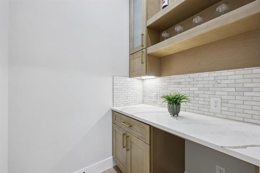 This space features a white countertop, subway tile backsplash, and light wood cabinetry with gold hardware