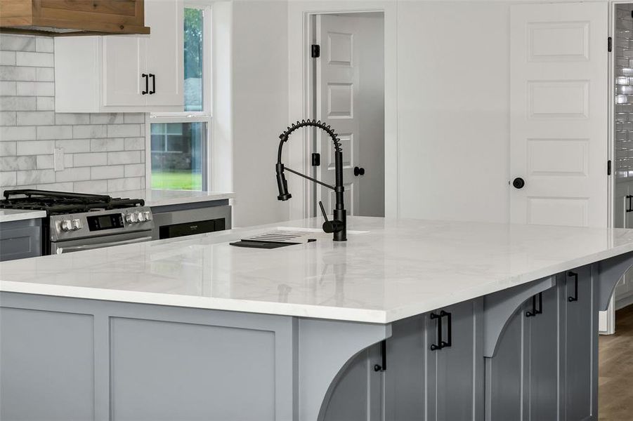 Kitchen featuring gray cabinetry, stainless steel gas stove, light stone counters, decorative backsplash, and under cabinet range hood Kitchen featuring gray cabinetry, stainless steel gas stove, light stone counters, decorative backsplash, and under cabinet range hood