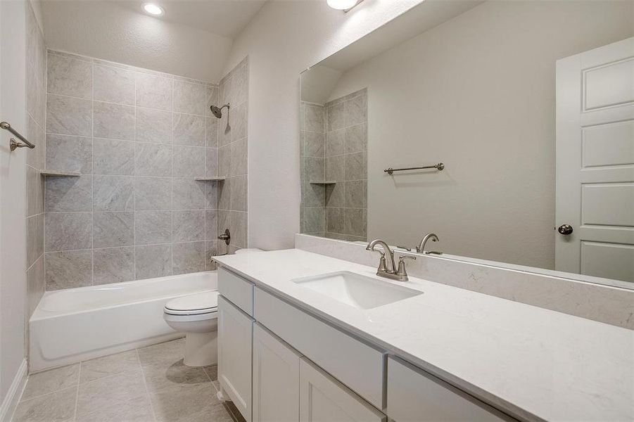 Full bathroom with tiled shower / bath combo, tile patterned floors, toilet, and vanity