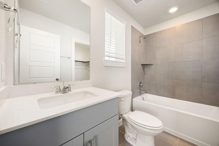 The secondary bathroom offers tile flooring, a bath/shower combination with a stylish tile surround, rich stained wood cabinetry, elegant light countertops, a mirror, and sleek fixtures with modern finishes. The secondary bathroom offers tile flooring, a bath/shower combination with a stylish tile surround, rich stained wood cabinetry, elegant light countertops, a mirror, and sleek fixtures with modern finishes.