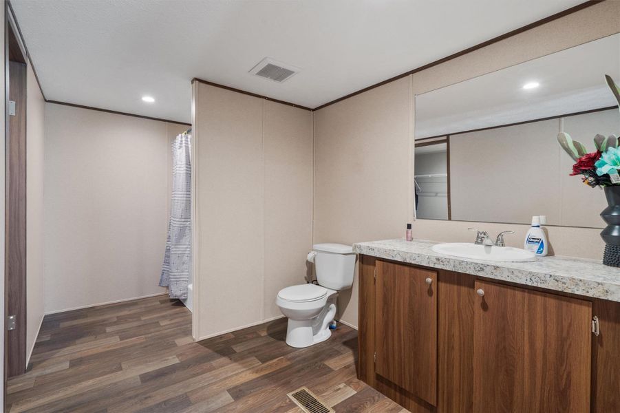 Laminate wood flooring and a stone-look vanity top anchor this functional, split-layout bathroom space.