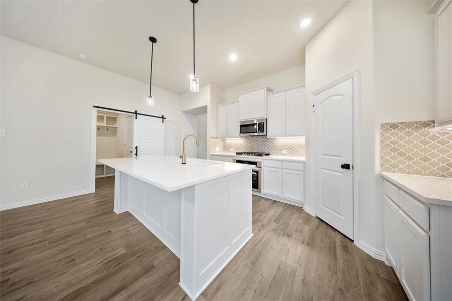 Kitchen featuring a barn door, tasteful backsplash, light wood-style floors, white cabinets, and light countertops