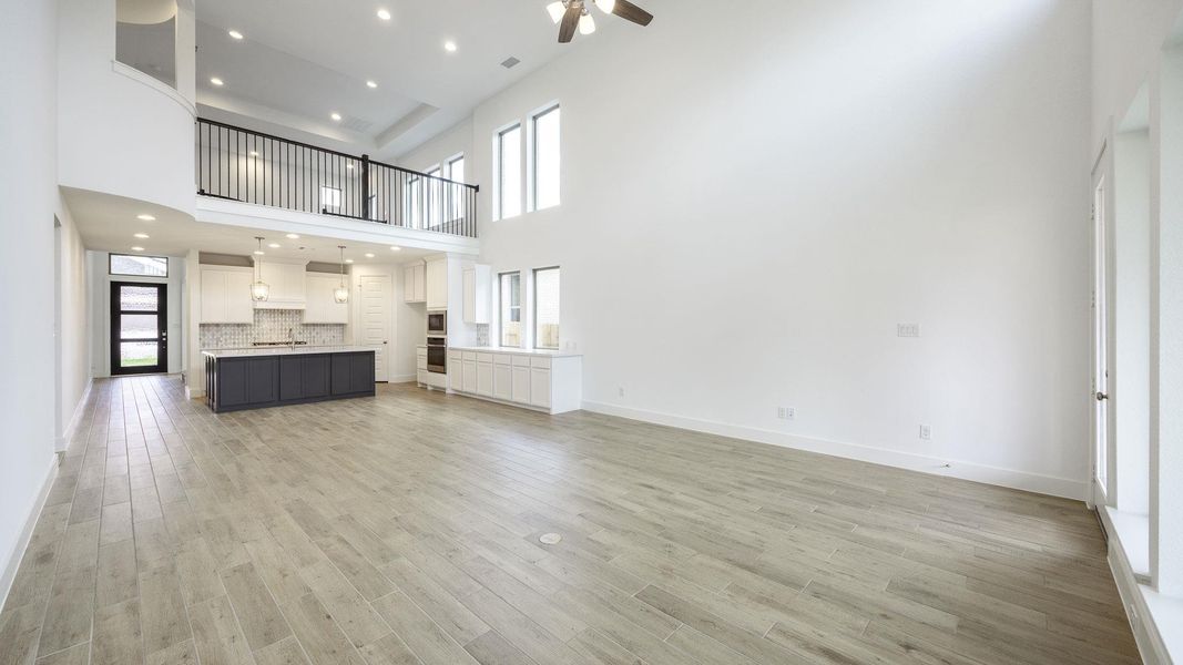 Unfurnished living room featuring a ceiling fan, a towering ceiling, light wood-style flooring, a sink, and baseboards Unfurnished living room featuring a ceiling fan, a towering ceiling, light wood-style flooring, a sink, and baseboards