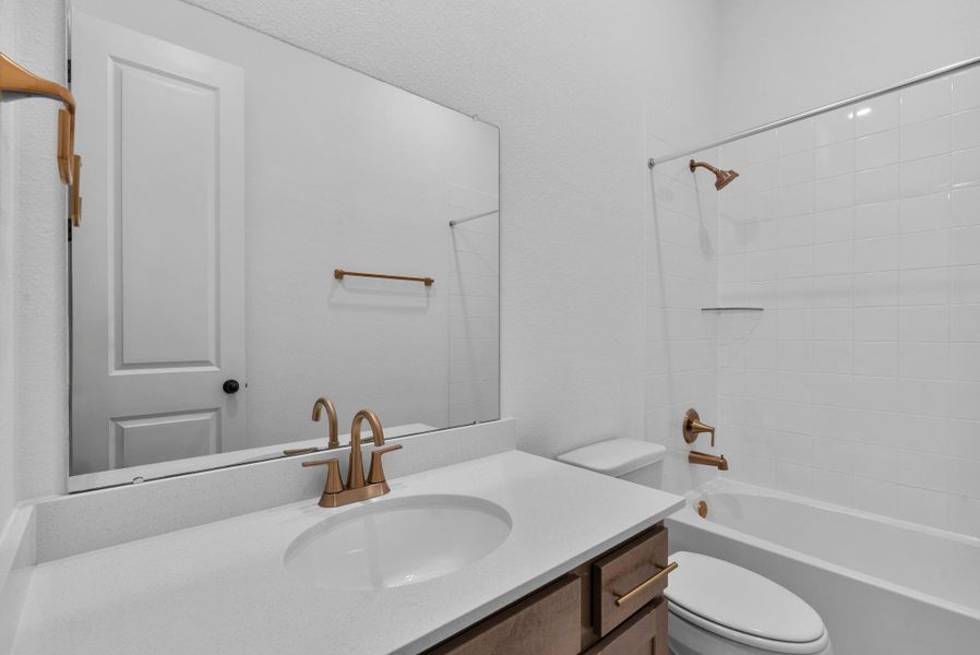 Stylish secondary bath featuring the AW Collection Laguna with stained cabinetry and light countertops with brass fixtures and a shower/tub combo.
